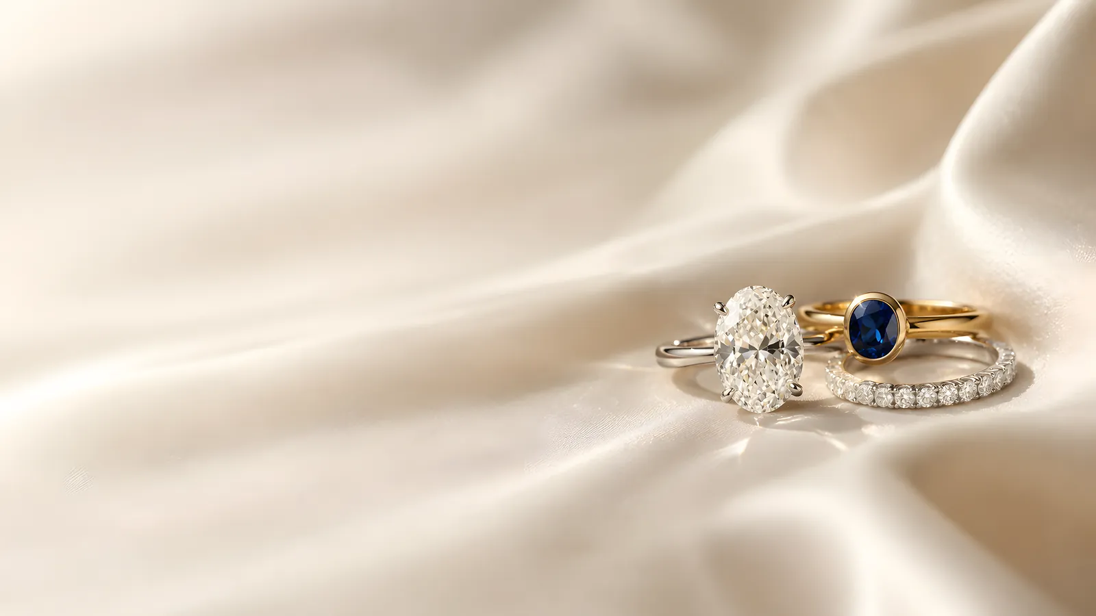 Oval diamond solitaire, sapphire band and pavé eternity band resting on ivory silk